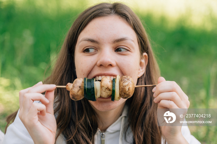 Teenager girl eating grilled vegetables outdoors. Vegan picnic with mushrooms and zucchini