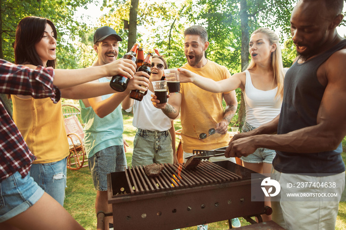 Group of happy friends having beer and barbecue party at sunny day. Resting together outdoor in a fo