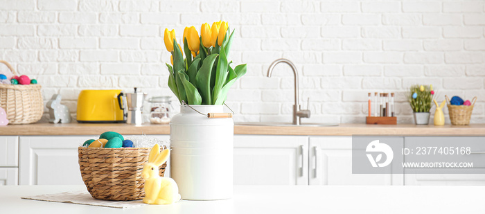 Wicker basket with Easter eggs, rabbit and bouquet of tulips on dining table in light kitchen