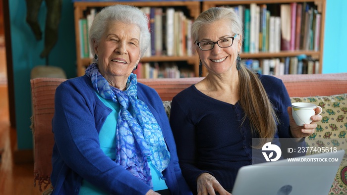 Portrait front view of smiling elderly mother and mature woman sitting on the sofa and shopping onli