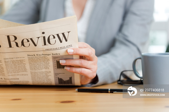 Close-up shot of businesswoman reading newspaper at office desk