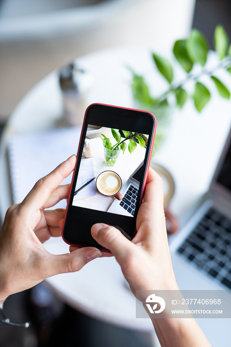 Hands of young female holding smartphone over table while photographing