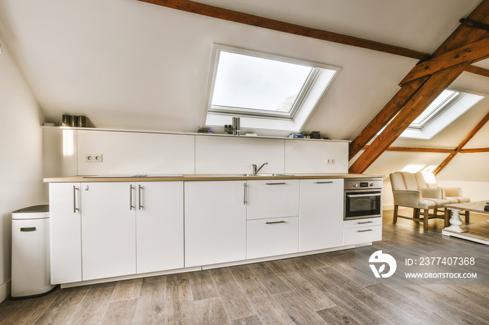 a kitchen and living room in an attic style home with wood flooring, white cabinets and light fixtur