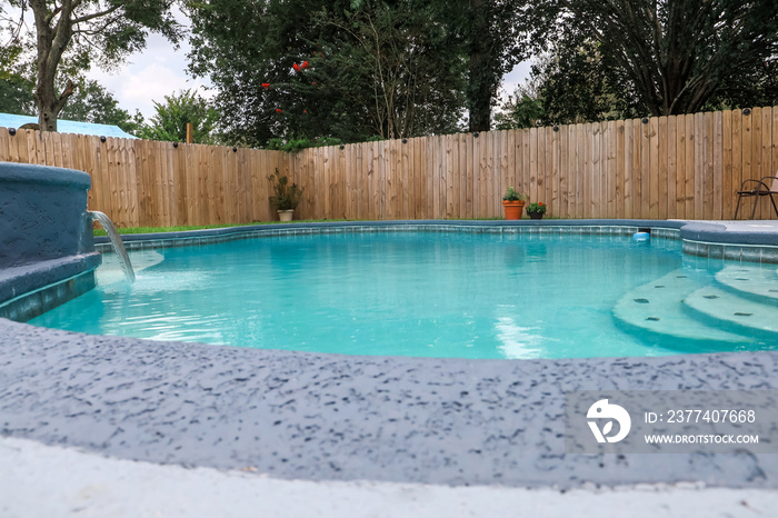 Low angle view of a large free-form gray grey accent swimming pool with turquoise blue water in a fe