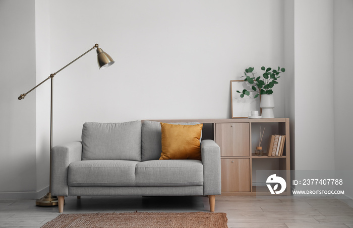 Interior of light living room with grey sofa, lamp and shelving unit