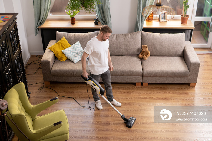 Young man doing domestic work while cleaning floor with vacuum cleaner