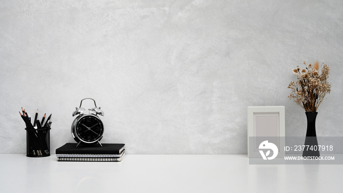 Minimal workplace with pencil holder, books, alarm clock and dried flower pot on white table