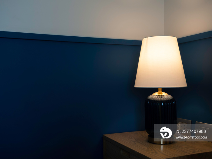 Luxury table lamp with white fabric, blue glass, and gold color materials shining on dark blue wall 