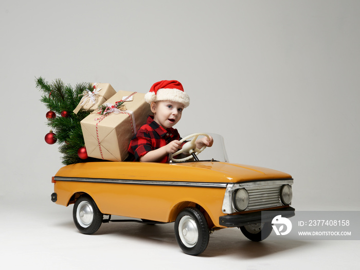 Small child boy in winter sitting in a yellow  retro toy car pulls on Christmas tree decorated