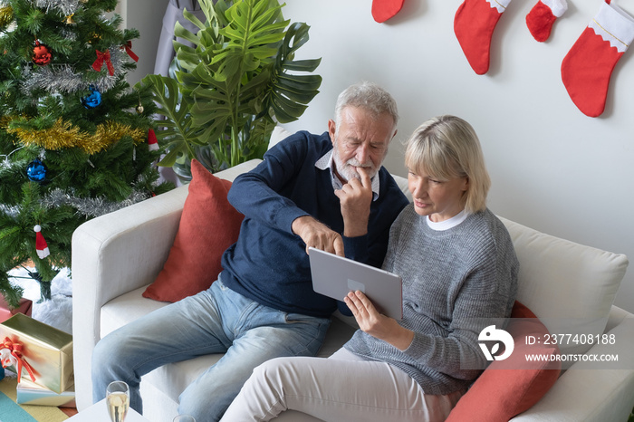 senior elderly caucasian old man and woman sitting on sofa, using and play internet tablet together 