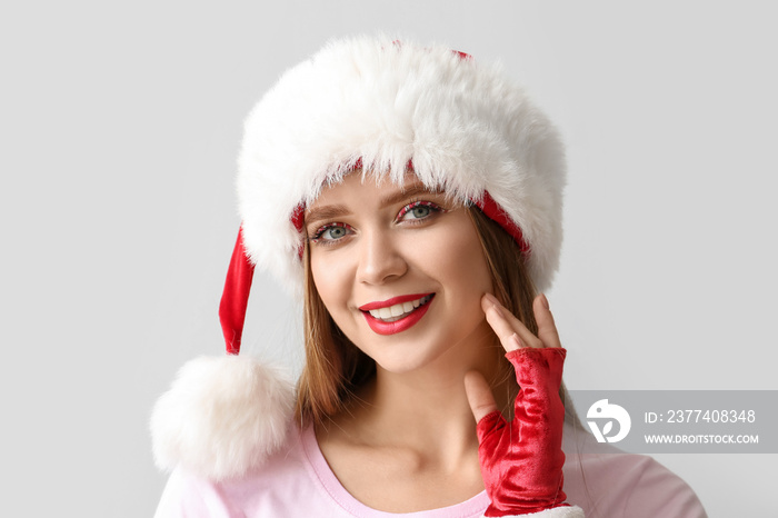 Beautiful young woman in Santa hat on grey background