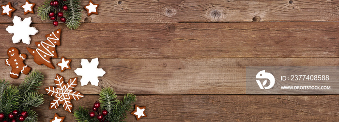 Christmas gingerbread cookies and tree branches. Above view corner border banner on a rustic wood ba