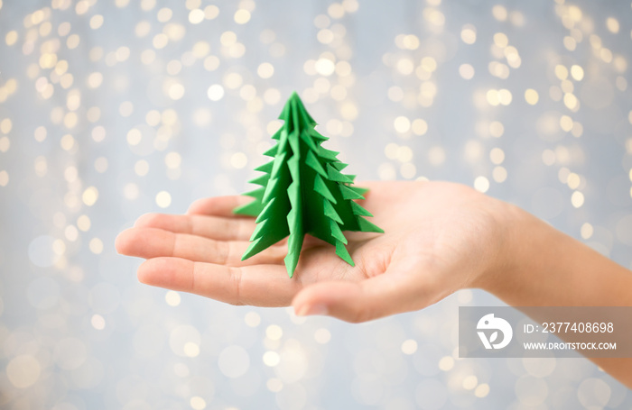 winter holidays, new year and craft concept - hand holding green paper origami christmas tree over f