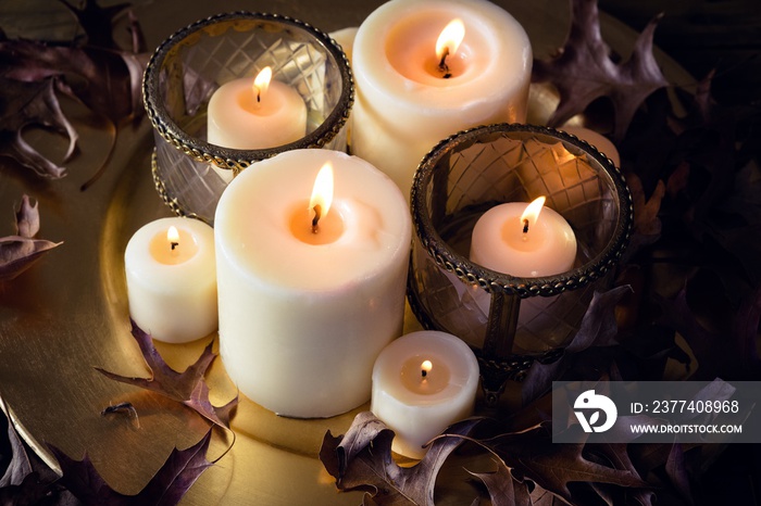 Lit candles and dry leaves on table