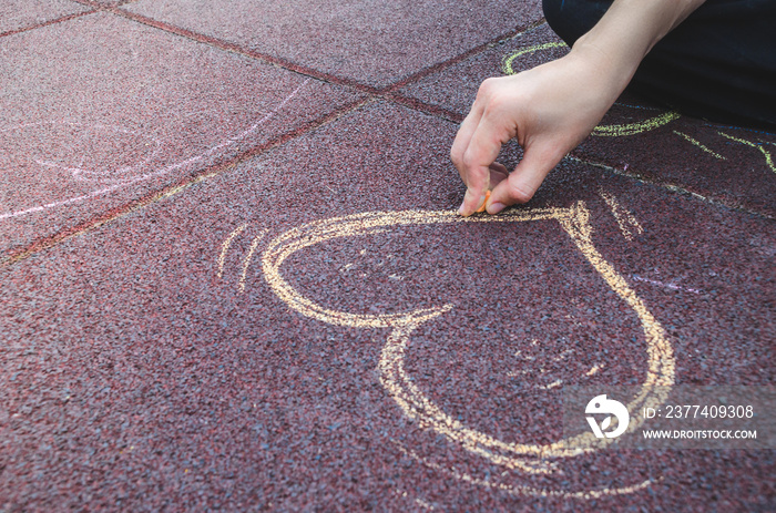 Female hand is drawing heart with a chalk in color