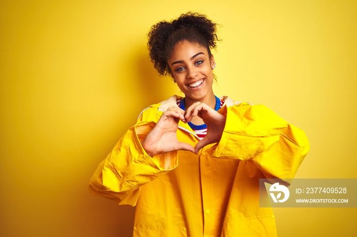 Young african american woman wearing rain coat over isolated yellow background smiling in love showi