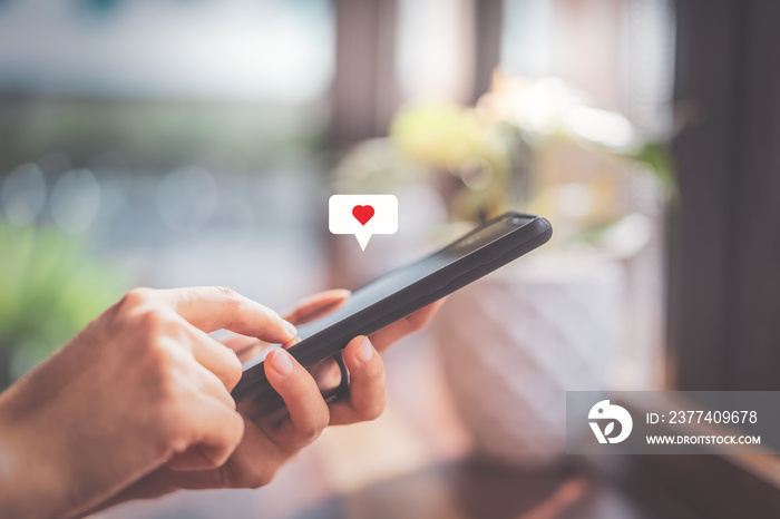 Woman hand using smartphone with heart icon at coffee shop background. Technology business and socia