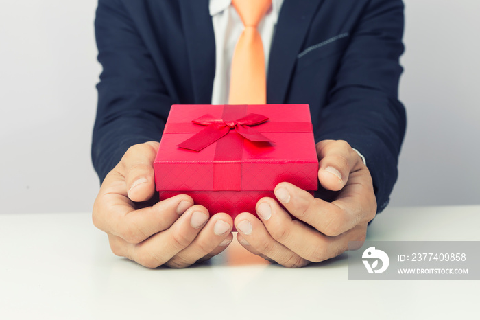 Businessman holds out the gift red box, isolated background