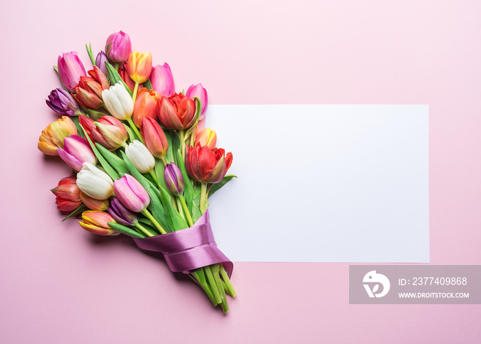 Colorful bouquet of tulips and a paper on pink background.