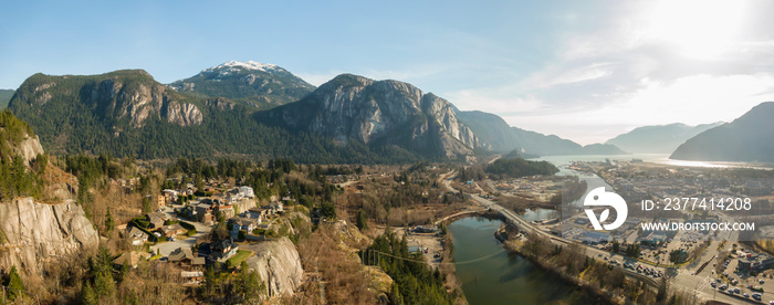 Aerial panoramic view of a small town with Chief Mountain in the background during a sunny day. Taken in Squamish, North of Vancouver, British Columbia, Canada.