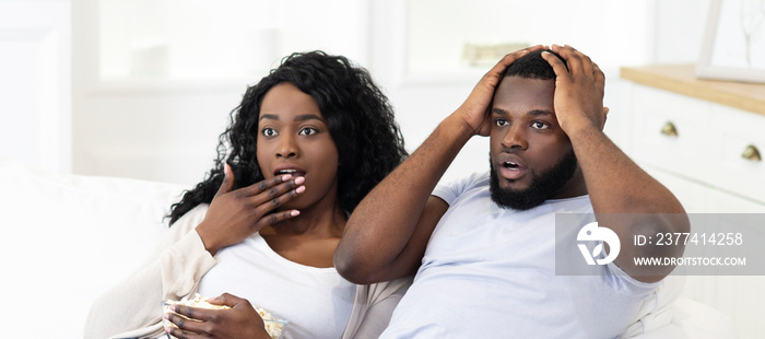 Emotional black couple watching horror movie on tv