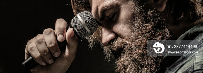 Man with a beard holding a microphone and singing. Bearded man in karaoke sings a song into a microphone. Male attends karaoke. Bearded man singing with microphone