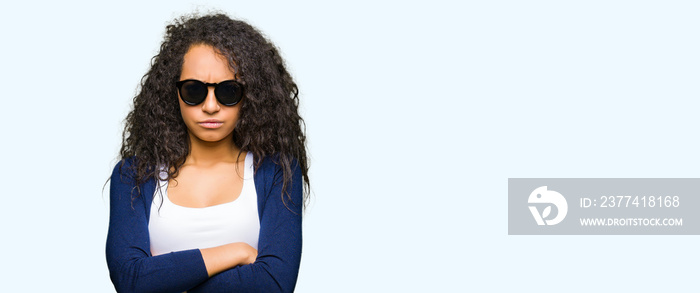 Young beautiful girl with curly hair wearing fashion sunglasses skeptic and nervous, disapproving expression on face with crossed arms. Negative person.