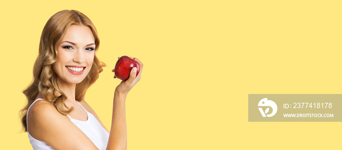 Portrait of happy smiling amazed woman holding red apple, over yellow color background. Blond girl in healthy eating, dieting and dental care, stomatology studio concept.