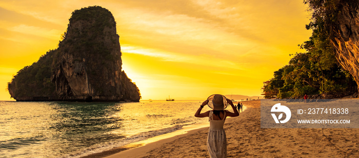 Woman tourist in white dress and hat walking on Phra nang Cave Beach at sunset, Railay, Krabi, Thailand. vacation, travel, summer, Wanderlust and holiday concept