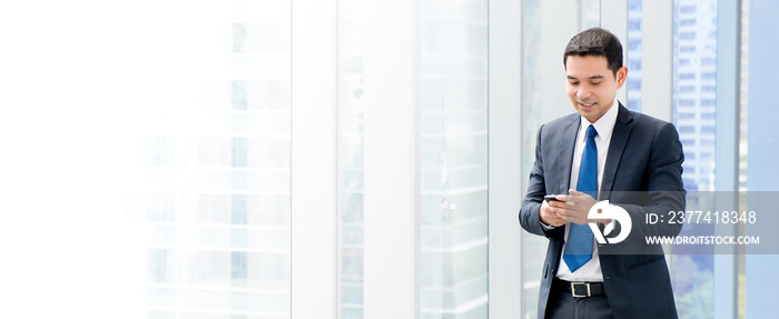 Asian businessman standing and using smartphone at office building hallway