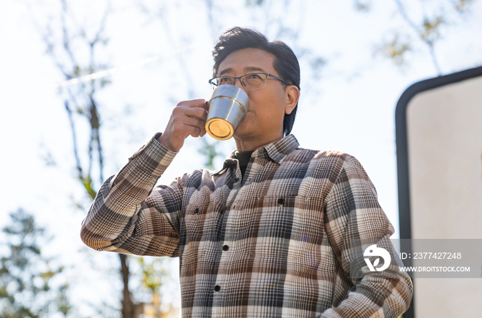 一个老年男人站在房车前喝咖啡