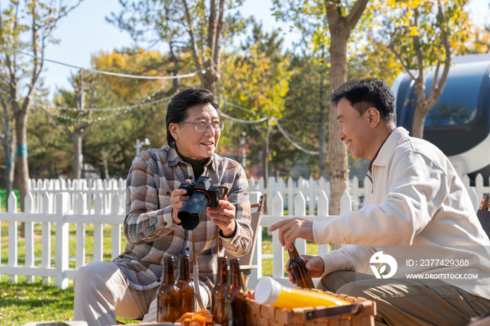 两个老年男人坐在露营地看数码相机