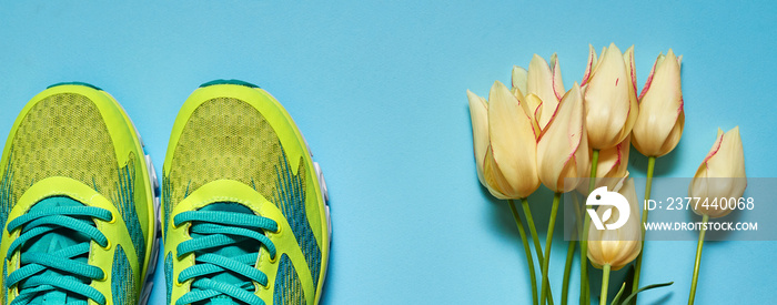 Pair of sport shoes and yellow tulips bouquet on colorful pastel background. New sneakers on blue paper, copy space. Overhead shot of running foot wear. Top view, flat lay