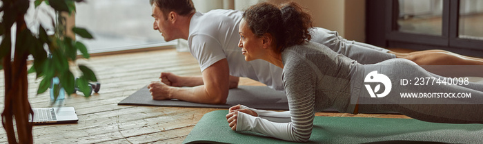 Athletic man and woman are doing core workout at home while watching online video on notebook