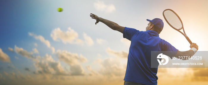 professional male tennis player in blue shirt hitting ball with racket on sunset sky background. banner copy space