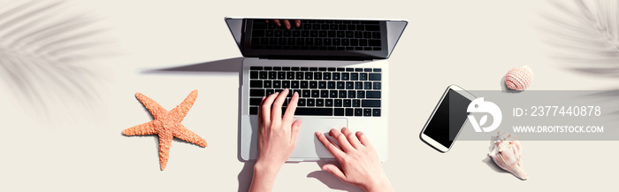 Person using a laptop computer with shells and starfish - flat lay