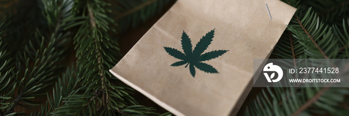 Paper bag with marijuana lying among green christmas tree branches closeup