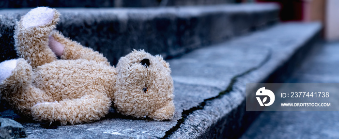 Lost childhood, loneliness and pain concept. Dirty teddy bear lying down outdoors. Horizontal image. Copy space for text.