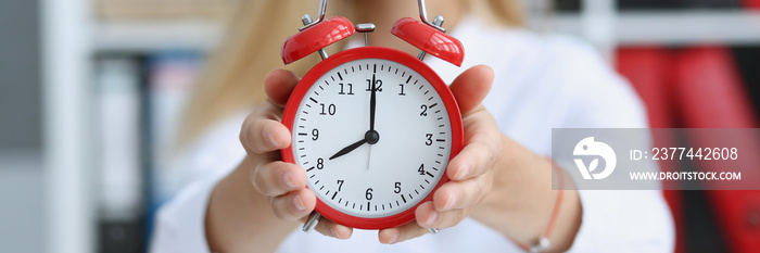 Smiling business woman holding in hand on the alarm clock a red color showing eight o’clock in the morning or evening AM PM