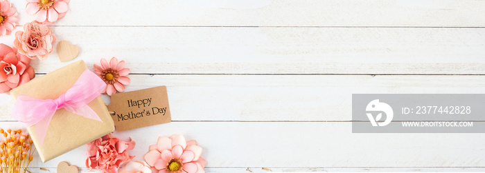 Happy Mothers Day corner border with paper flowers, gift box and tag. Overhead view against a white wood banner background. Copy space.