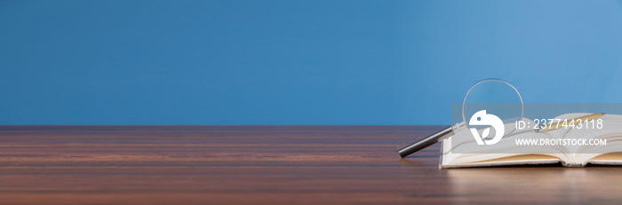 open book with magnifying glass on wooden desk in information library of school or university, concept for education,reading , study, copy space and banner background.