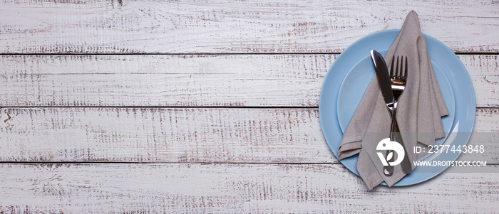 Blue plates, napkin and cutlery on an old white wooden background.