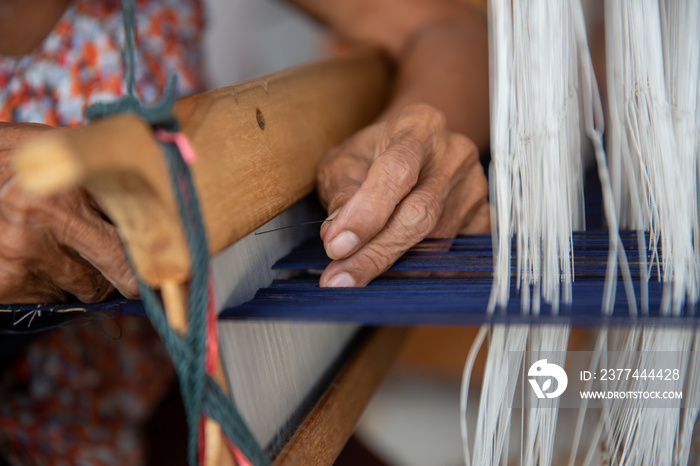 Cotton weaving. Close-up woman hand weaving cotton on manual loom. Thai cotton handmade. Homespun fabric process. The process of fabric weaving in vintage weaver machine. Selective focus.