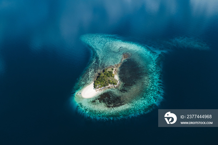 Tropical background and travel concept. Aerial view of small uninhabited island from above. Coral reef and white sand beach.