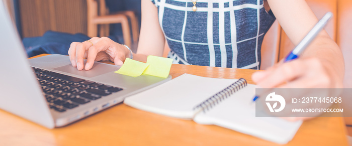 Woman hand working at a computer and writing on a notepad with a pen in the office.Web banner.