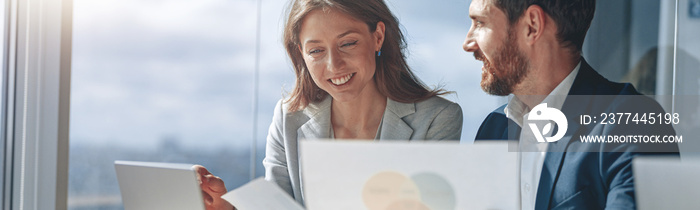 Two business people in office explaining statistics data to each other looking at documents