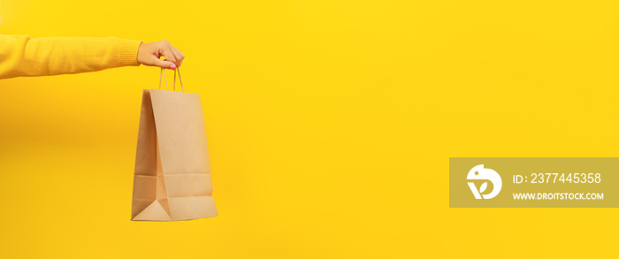 Woman hand holding paper shopping bag on yellow background. Discounts and sale of concept. Panoramic image