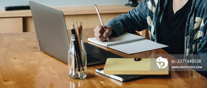 Cropped photo of woman writing making list taking notes in notepad working or learning on laptop indoors- educational course or training, seminar, education online concept