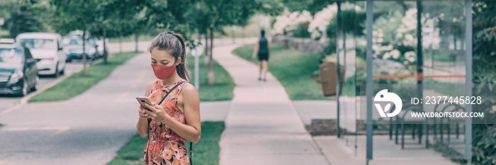 Mask wearing woman waiting for the bus holding mobile phone contact tracing app when using public transport. Panoramic banner crop of Asian girl using cellphone outside while walking.