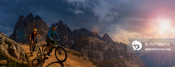 Cycling outdoor adventure in Dolomites. Cycling woman and man  on electric mountain bikes in Dolomites landscape. Couple cycling MTB enduro trail track. Outdoor sport activity.